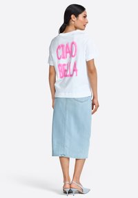 White t-shirt with pink "CIAO BELLA" text on back, paired with a light blue denim midi skirt and blue heels. Smooth fabric, relaxed fit.