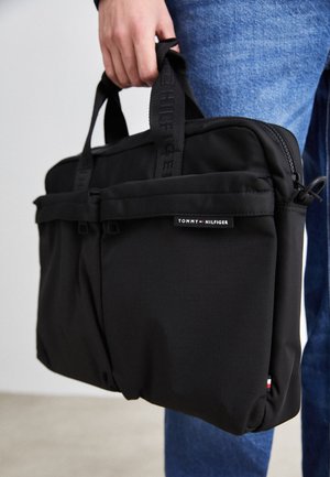 Fekete laptop táska dupla elülső zsebbel, textúrált anyagból készült, webes fogantyúkkal és Tommy Hilfiger logóval ellátva.
