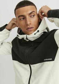 Giacca con cappuccio caratterizzata da un design a blocchi di colore bianco e nero, realizzata in tessuto liscio. Include un cordino sul cappuccio e il logo del marchio.
