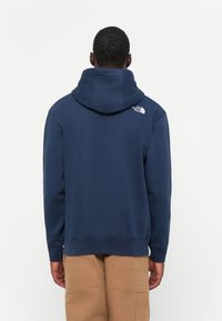 Marineblauwe hoodie met een kangoeroezak en geribbelde manchetten. Bevat een klein wit logo op de bovenrug. Gemaakt van een katoenmix.