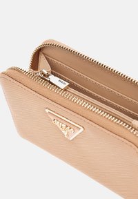 Portafoglio zip beige chiaro realizzato in materiale testurizzato. Presenta hardware in tonalità oro e un logo triangolare sulla parte anteriore. Scomparto interno visibile.