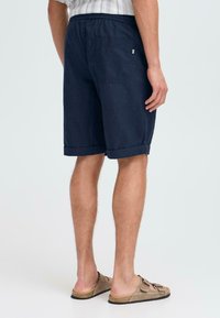 Marineblaue Shorts aus leichtem Material, mit einem Kordelzug in der Taille, umgeschlagenen Säumen und einer Gesäßtasche auf der rechten Seite.