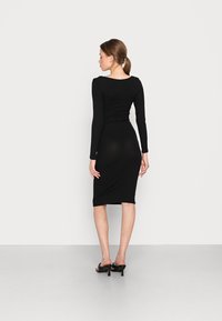 Vestido midi preto de mangas longas com um design ajustado, textura suave e decote quadrado, combinado com sapatos de salto alto pretos.