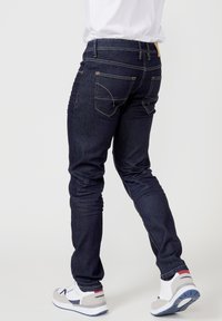 Dunkelblaue Jeans aus Denim mit schlankem Fit, ausgestattet mit gelben Nähten, zwei Gesäßtaschen und einem passenden hellbraunen Lederetikett am Bund.