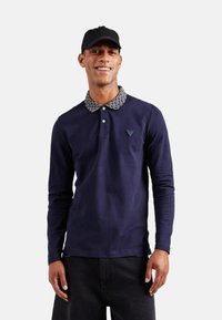 Polo de manga larga en color marino con cuello estampado y logotipo en el pecho. Hecho de algodón con una textura suave. Corte casual para un uso versátil.
