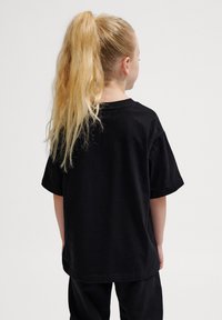 Sort bomulds T-shirt med korte ærmer, afslappet pasform, rund hals og flade sømme; set fra ryggen, båret af et barn med langt hår.