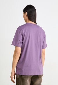 Lilla bomulls T-skjorte med korte ermer, rund hals og et enkelt design, vist fra baksiden, som viser en avslappet passform og myk tekstur.