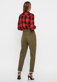 Camicia di flanella a quadri rossi e neri, pantaloni verdi a vita alta e sandali neri con tacco. La camicia presenta un colletto classico; i pantaloni hanno tasche posteriori.