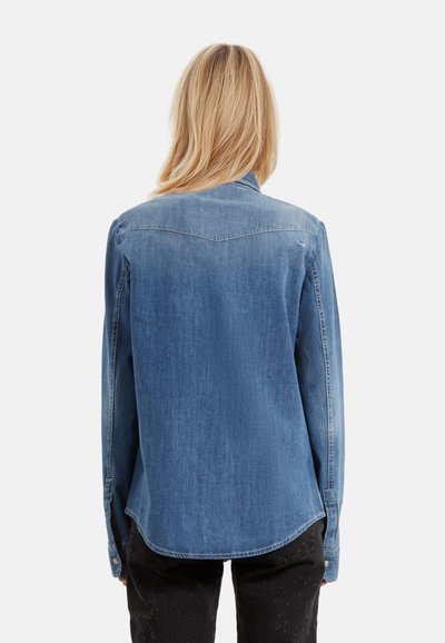 Camisa de mezclilla en azul medio con cuello puntiagudo, mangas largas y dobladillo curvado. Presenta yugo trasero y puños con botones.