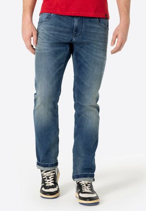 Blaue Jeans aus Denim mit einem verblassten Finish, geradem Beinschnitt, fünf Taschen und einem klassischen Bund. Getragen mit schwarz-weißen Turnschuhen.