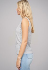Top gri fără mâneci, cu un model texturat de ochi de pisică, având o formă ajustată, purtat cu blugi skinny de un albastru deschis.