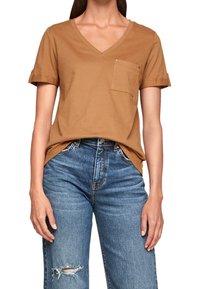 Brun bomull v-ringad t-shirt med uppvikta korta ärmar, en bröstficka och en avslappnad passform, tillsammans med slitna blå denimjeans.