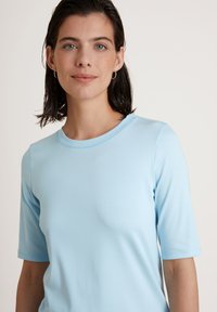 Lichtblauw kort mouwtop gemaakt van gladde stof, met een ronde halslijn en een getailleerde pasvorm. Eenvoudig ontwerp met minimale details.