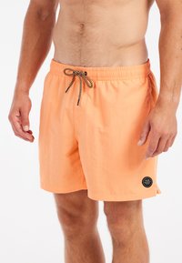 Shorts de bain légers, couleur pêche, avec une taille élastique, un cordon noir et un patch logo circulaire sur la cuisse. Texture lisse.