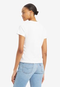Vit t-shirt med kort ärm och rund halsringning, tillsammans med ljusblå denimjeans som har en logotyp på bakfickan. Slät, enfärgad textur.