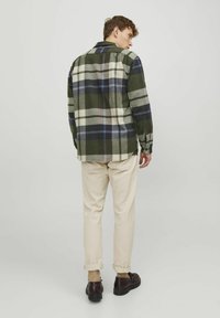Groene en beige geruite flanellen blouse met een relaxte pasvorm, gecombineerd met crèmekleurige broek en donkere schoenen. Heeft knoopdetails en opgerolde mouwen.