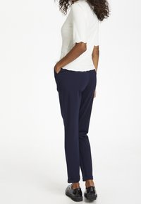 Biała, prążkowana bluzka z krótkimi rękawami w połączeniu z granatowymi, zwężającymi się spodniami. Spodnie mają boczne kieszenie i podwinięte mankiety. Całość dopełniają czarne buty.