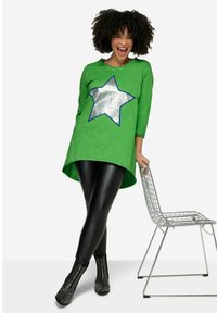 Tunique verte avec un motif d'étoile argentée, dotée de manches trois-quarts et d'un ourlet arrondi, associée à des leggings noirs et des bottines à clous.