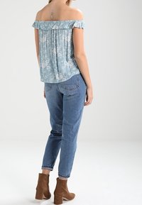 Světle modrý květinový top s odhalenými rameny a volánkovými okraji, spojený s modrými džíny s vysokým pasem a hnědými kotníkovými botami na podpatku.