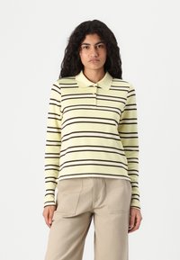 Lange mouw polo shirt in lichtgeel met horizontale bruine strepen, voorzien van een kraag, knoopsluiting en ribbeltextuur.