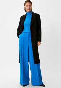 Czarny płaszcz, niebieski golf i szerokie niebieskie spodnie. Gładkie materiały, dopasowany krój, pionowe linie na golfie oraz spiczaste czarne buty.
