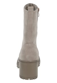 Botines de ante beige con tacón grueso, que cuentan con una cremallera en la parte trasera y detalle del logo en el tacón. Textura lisa sin patrones.