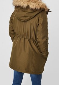 Olive green parka with a faux fur hood, adjustable drawstring waist, and snap button pockets. Smooth fabric with a relaxed fit.