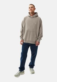 Grå hoodie med känguruficka och ribbade ärmar, parat med mörkblå jeans och ljusa sneakers. Enkel, avslappnad passform.