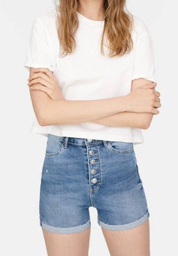 Vit bomulls t-shirt med korta ärmar, kombinerad med högmidjade, ljusblå denimshorts med fem knappar fram och uppvikta benslut.
