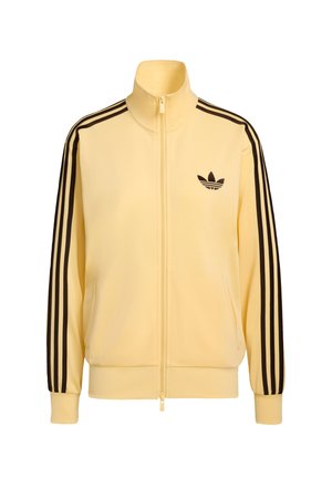 Κίτρινο μπουφάν με φερμουάρ, κατασκευασμένο από λείο ύφασμα, με μαύρες τρεις ρίγες στα μανίκια και μικρό μαύρο λογότυπο στο στήθος.