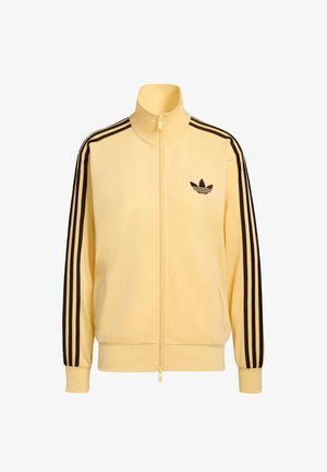 Kollane lukuga jakk, valmistatud siledast kangast, millel on mustad kolmetriibulised aktsendid varrukatel ja väike must logo rinnal.