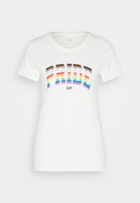 Bílá bavlněná tričko s multikolorovým grafickým prvkem "PRIDE" v tučných písmenech s duhovým designem. Logo značky "GAP" je umístěno níže.