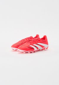 Røde fotballsko har en strømlinjeformet, teksturert overdel med svarte og hvite striper, plastspisser og en polstret krage for støtte.
