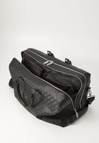 Bolso de viaje de cuero negro con un patrón tejido texturizado, cremalleras dobles, asas en la parte superior y correa ajustable para el hombro. Interior espacioso con forro oscuro.
