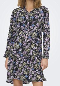 Abito a stampa floreale con sfondo blu navy, caratterizzato da fiori viola, blu e verdi, colletto con bottoni e maniche lunghe con polsini arricciati.
