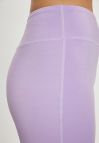 Magasan derekú, testhez simuló leggings világos levendula színben, rugalmas anyagból készült. Lapolt varrással készült, ami kényelmes viseletet és sima textúrát biztosít.