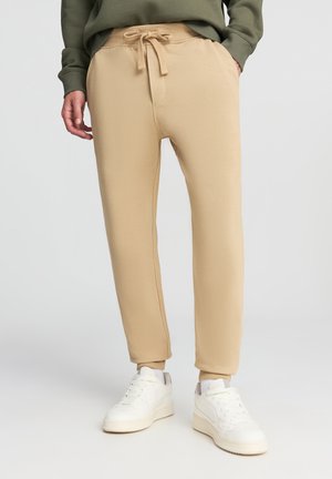 Pantaloni jogger beige realizzati in tessuto morbido, con vita elastica e coulisse, gambe affusolate e polsini a coste.