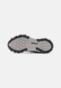 Suela de zapatilla de trail Columbia con un diseño de goma negra y gris, que presenta patrones de tracción hexagonales para agarre y tracción en diversas superficies.