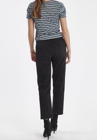 Jeans negros de tiro alto con corte recto, combinados con una camiseta a rayas azul y gris, ambos hechos de tela suave.