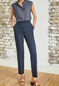 Pantalon bleu marine foncé ajusté avec une texture lisse, associé à un chemisier gris à manches courtes, col, avec boutons et poches poitrine.