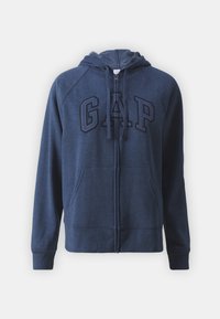 Sudadera azul marino con cremallera frontal, capucha con cordón y gran logo bordado de "GAP" en un color contrastante. Cuenta con bolsillos tipo canguro.