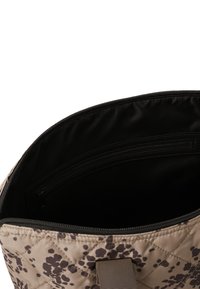 Gepatchte beige Tasche mit dunklem Sprenkelmuster, die ein schwarzes Innenfutter und eine Reißverschlusstasche für die Organisation bietet. Tragegriffe für den Transport.