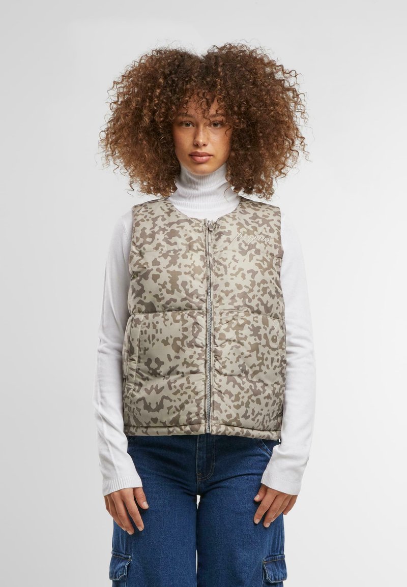 Gepolsterte Weste in einem gedämpften Khaki- und Braun-Tarnmuster, mit Reißverschluss, hohem Kragen und ausgestelltem Saum. Getragen über einem weißen Rollkragenpullover.