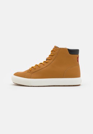Zapatillas altas hechas de material sintético texturizado en tono marrón. Presentan un cuello negro, cordones naranjas y una suela de goma blanca con un patrón de tracción marrón.