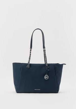 Sac cabas Michael Kors bleu foncé avec chaînes et bandoulières en cuir ainsi qu’un pendentif logo circulaire sur fond blanc.