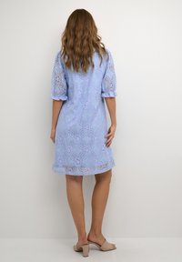 Ljust blå spetsklänning med korta puffärmar, blommönster, v�ågig nederkant och semi-transparent struktur. Bärs med beige klacksandaler.