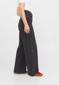 Breda svart denimbyxor med hög midja, med en klassisk femficksdesign och kontraststygn. I kombination med röda sneakers.