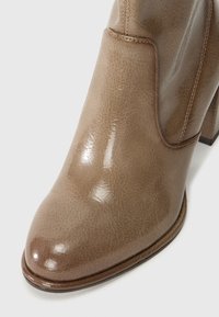Brown ankle boot made of glossy synthetic material with a rounded toe, block heel, and subtle texture, featuring contrasting stitching details.