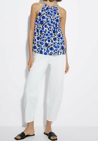 Top halter floreale in blu e bianco, con scollatura arricciata e spalline sottili. Abbinato a pantaloni bianchi lunghi e sandali neri a scivolo.