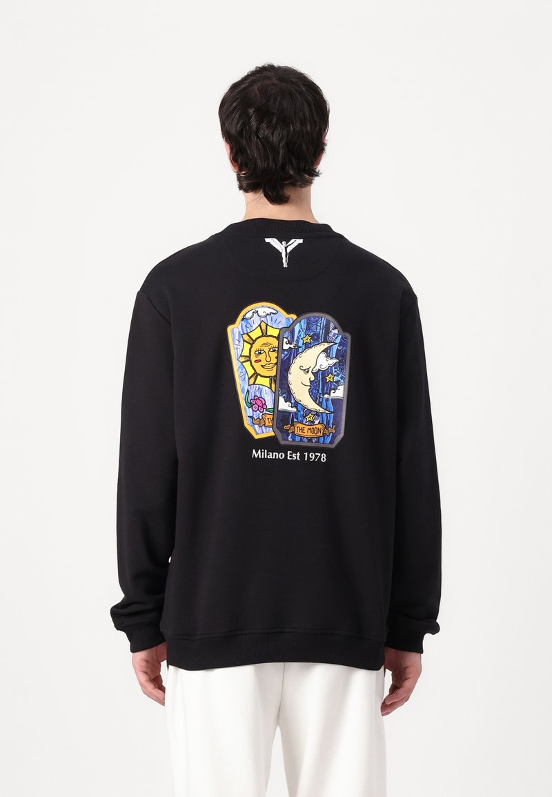 Black sweatshirt featuring colorful graphic design on the back with sun and moon motifs. Text "Milano Est 1978" below the artwork. Soft texture.